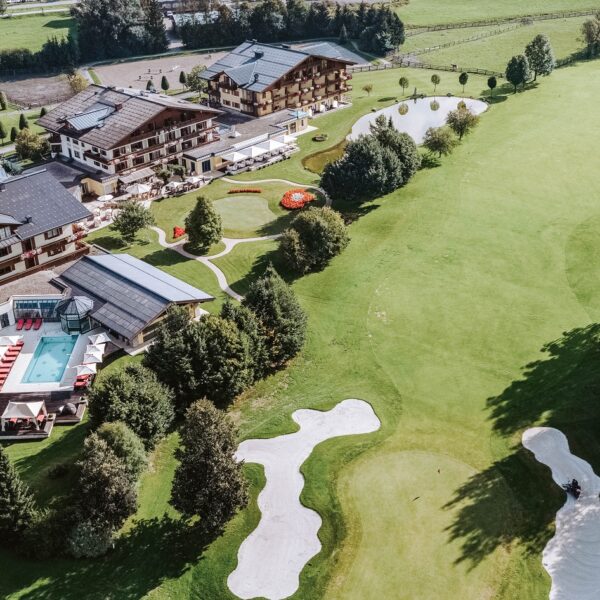 Luftaufnahme eines Resorts mit einem Pool, umliegenden Gärten, kleinen Teichen und einem angrenzenden Golfplatz mit Sandbunkern und grünen Fairways.