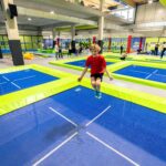 Kinder springen auf großen blauen Trampolinen im JUMP DOME Salzburg, einem Indoor-Trampolinpark. Im Hintergrund sind Erwachsene und andere Kinder zu sehen.