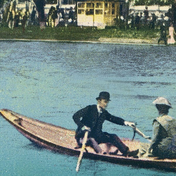 Zwei Menschen in zeitgenössischer Kleidung rudern in einem schmalen Holzboot auf einem Fluss. Im Hintergrund sind auf dem grasbewachsenen Ufer eine Menschenmenge und ein gelbes Gebäude zu sehen.