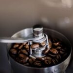 Nahaufnahme von Kaffeebohnen in einer manuellen Kaffeemühle mit einem Metallgriff, bereit zum Mahlen.