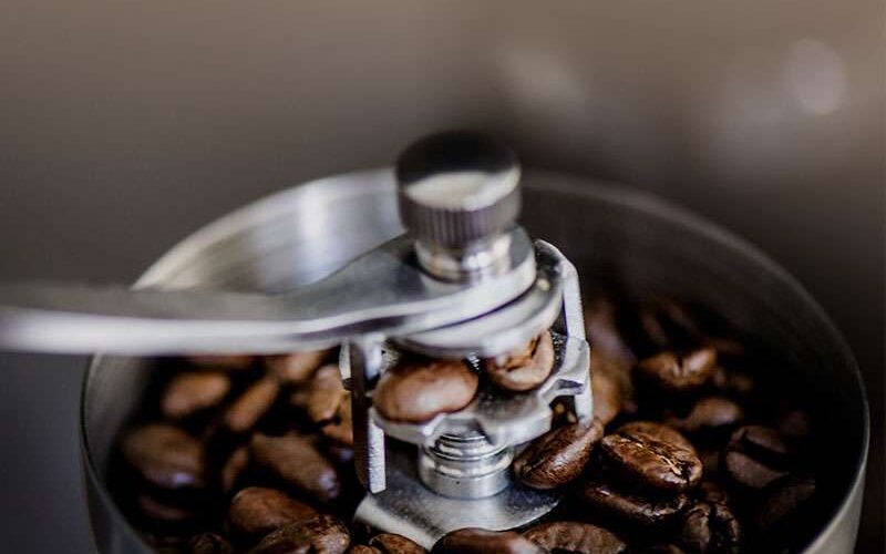 Nahaufnahme von Kaffeebohnen in einer manuellen Kaffeemühle mit einem Metallgriff, bereit zum Mahlen.