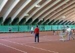 In einer großen Tennishalle mit einem gewölbten Dach wird auf mehreren Plätzen Tennis gespielt und unterrichtet.