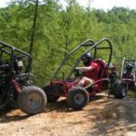 Drei Personen mit Helmen fahren auf einem unbefestigten Weg, der von grünen Bäumen und Pflanzen umgeben ist, Go-Karts.