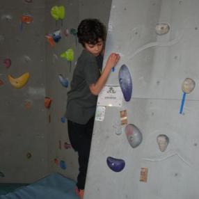 Ein Junge klettert an einer Indoor-Boulderwand, hält sich an bunten Griffen fest und steht auf einer blauen Matte.