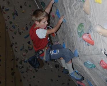 Ein Junge klettert mit einem Klettergurt an einer Indoor-Kletterwand und hält sich an bunten Griffen fest.