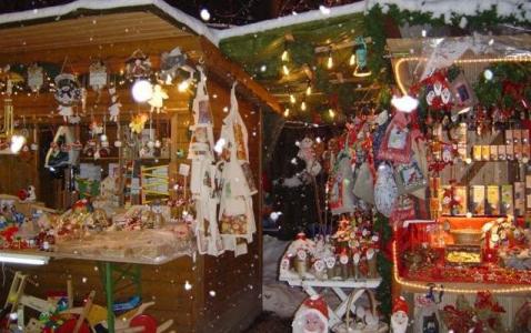 Zwei hölzerne Marktstände, die mit Weihnachtsschmuck und Lichtern geschmückt sind, bieten verschiedene Weihnachtsartikel und Geschenke an, während in der Szene sanft der Schnee fällt.