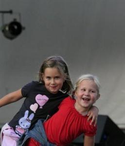 Zwei junge Mädchen lächeln und posieren zusammen vor einem grauen Hintergrund. Die eine trägt ein schwarzes Shirt mit einer Hasengrafik, die andere ein rotes Shirt.