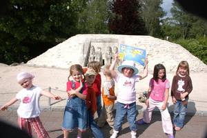 Eine Gruppe von sieben Kindern posiert und lächelt an einem sonnigen Tag vor einer Sand- oder Steinskulptur im Freien.