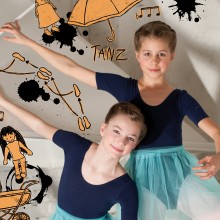 Zwei junge Balletttänzerinnen in blauen Trikots und blaugrünen Tutus posieren mit erhobenen Armen vor einer Wand, die mit Illustrationen zum Thema Tanz geschmückt ist.