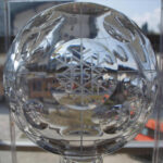 Nahaufnahme einer Trophäe aus Klarglas mit geätztem Schneeflockenmuster, die in einem Innenraum mit Fenstern und einer Außenlandschaft im Hintergrund ausgestellt ist.