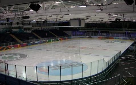 Eine leere Eishockeyhalle mit Sitzgelegenheiten rund um das Eis und Schutznetzen über den Banden.