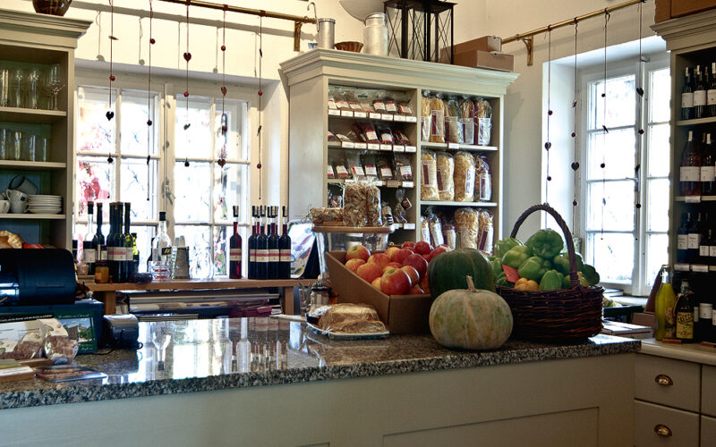 Ein Lebensmittelladen mit einer Auslage mit frischen Produkten, Backwaren, Weinflaschen und Regalen mit Nudeln und verpackten Waren im Hintergrund.