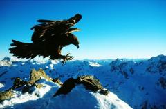 Ein großer Adler stürzt sich mit ausgefahrenen Krallen über eine verschneite Berglandschaft unter einem klaren blauen Himmel.