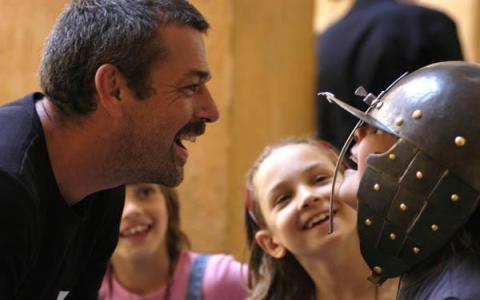 Ein Mann lächelt und spricht mit einem Kind, das einen Metallhelm trägt, während zwei andere Kinder im Hintergrund lächeln.