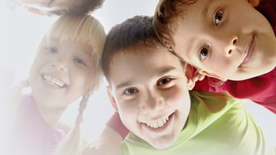 Drei Kinder, die lächelnd in die Kamera schauen, mit hellem Licht im Hintergrund.