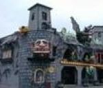 Eine dunkle, schlossähnliche Vergnügungsparkattraktion mit steinähnlichen Wänden, gruseligen Dekorationen und bunten Lichtern an der Außenseite.