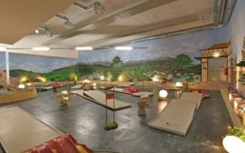 Indoor-Minigolfplatz mit mehreren Putting-Greens und Hindernissen, dekoriert mit Pflanzen, Laternen und einem Wandgemälde mit einer malerischen Landschaft an der Rückwand.