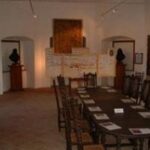 Ein Konferenzraum mit einem langen Tisch, Holzstühlen, Dokumenten auf dem Tisch, Kunstwerken an den Wänden und zwei Büstenskulpturen auf Sockeln.