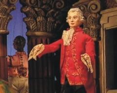 Eine Puppe in einem verzierten roten Mantel mit weißer Spitze steht vor detaillierten architektonischen Säulen.