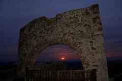 Im Vordergrund steht ein steinerner Torbogen, durch den ein Sonnenuntergang vor einem sich verdunkelnden Himmel zu sehen ist.