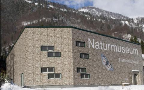 Ein modernes Backsteingebäude mit der Aufschrift "Naturmuseum Treffpunkt Natur" und dem Bild eines Schmetterlings in einer verschneiten Berglandschaft.