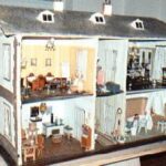 Ein zweistöckiges Puppenhaus mit detaillierten Miniaturmöbeln und -dekorationen, das verschiedene Räume wie Küche, Wohnbereich und Schlafzimmer zeigt.