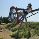 Eine Person schwingt auf einer großen Seilschaukel in einem Park mit Grünflächen und Menschen im Hintergrund.