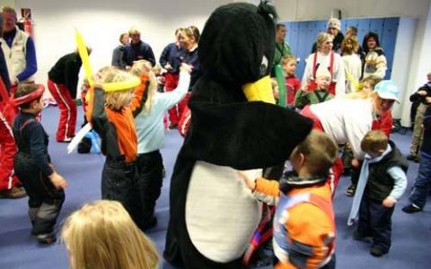 Kinder und Erwachsene versammeln sich im Haus und spielen um eine Person in einem großen Pinguinkostüm.