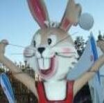 Große Cartoon-Kaninchen-Statue mit erhobenen Armen, in rotem Outfit, im Freien in der Nähe eines weißen Zeltes und eines Metallzauns.