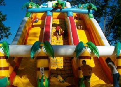 Kinder klettern und spielen auf einer großen, aufblasbaren Dschungelrutsche mit Palmendekoration.