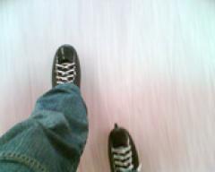 Eine Person in dunklen Schlittschuhen und blauen Jeans, die auf einer Eisbahn Schlittschuh läuft.