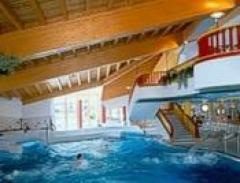 Hallenbadbereich mit Holzdecke, großen Fenstern, Treppen und Menschen, die im Wasser schwimmen.