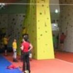 Mehrere Kinder und Erwachsene nehmen am Indoor-Klettern an den bunten Kletterwänden in einer Sporthalle teil.