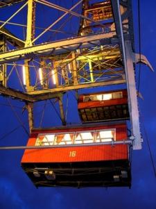 Zwei rot beleuchtete und mit Nummern versehene Riesenradkabinen, von unten gesehen vor einem tiefblauen Abendhimmel.