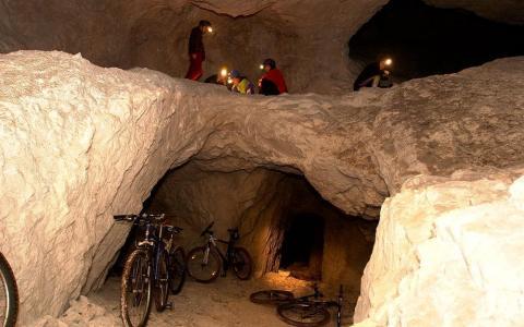 Mehrere Personen mit Stirnlampen erkunden eine felsige Höhle mit mehreren Fahrrädern, die an den Wänden und am Boden der Höhle lehnen.
