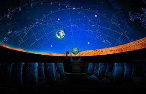 Sitzreihen mit Blick auf eine Kuppel mit einer projizierten Sternenkarte und Sternbildern in einem dunklen Planetarium.