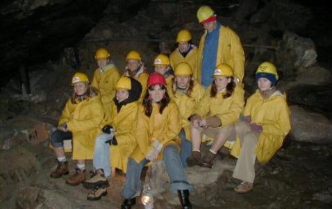 Eine Gruppe von Menschen in gelben Regenmänteln und Schutzhelmen sitzt und steht auf Felsen in einer schwach beleuchteten Höhle.