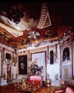 Verziertes Zimmer im Barockstil mit kunstvollen Deckenfresken, goldverzierten Möbeln und einem zentralen Bett in Rosa und Gold unter einer reich verzierten Decke.