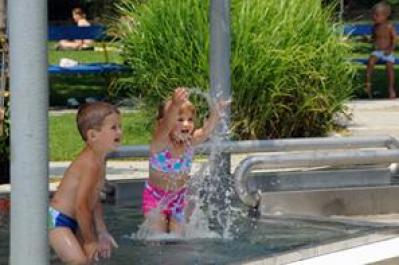 Zwei kleine Kinder in Badeanzügen spielen und planschen an einem sonnigen Tag am Rande eines flachen Freibads.
