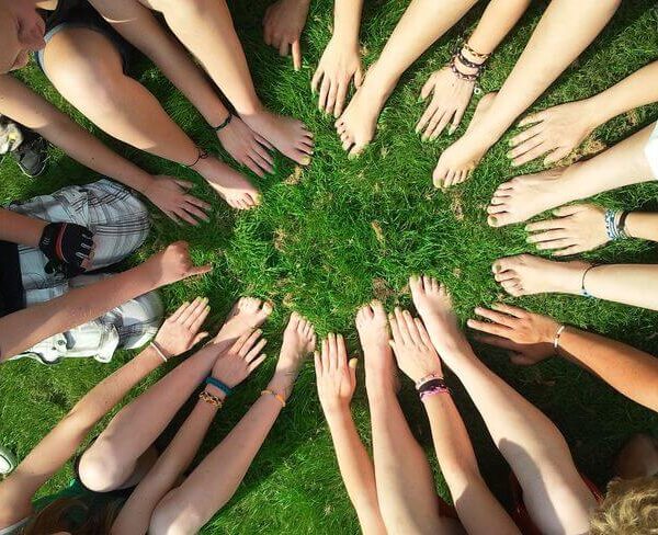 Eine Gruppe von Menschen sitzt im Kreis auf einer Wiese und streckt ihre Hände und nackten Füße in die Mitte.