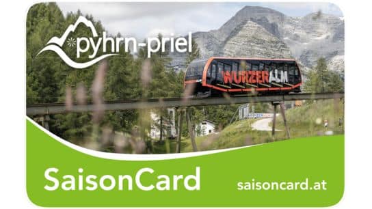 Eine Standseilbahn fährt auf erhöhten Gleisen in einer bergigen, bewaldeten Gegend mit der Aufschrift "Wurzeralm" an der Seite. Auf der Karte steht "pyhrn-priel SaisonCard" und zeigt eine Website.