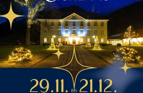 Ein großes Gebäude, das nachts mit Weihnachtslichtern und -bäumen geschmückt ist, mit den Veranstaltungsdaten "29.11. bis 21.12." am unteren Rand.